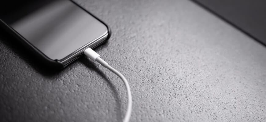 Prie įkroviklio prijungtas išmanusis telefonas, rodantis krovimo indikatorių