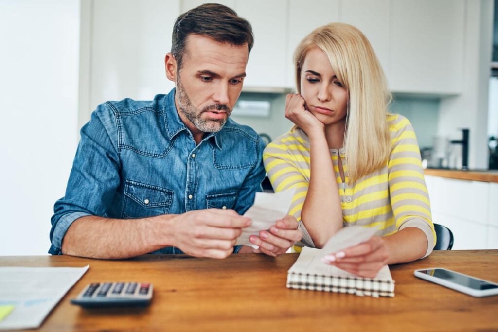 Sad couple looking at store receipt while managing home finances worried about money